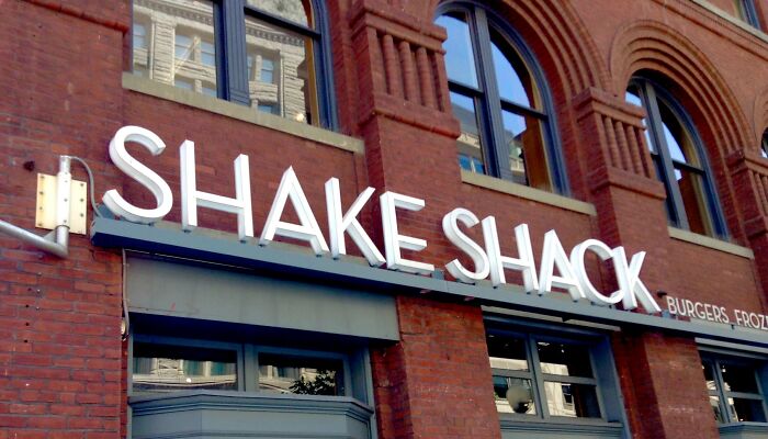 Shake Shack sign on a brick building exterior, associated with hyped fast foods.