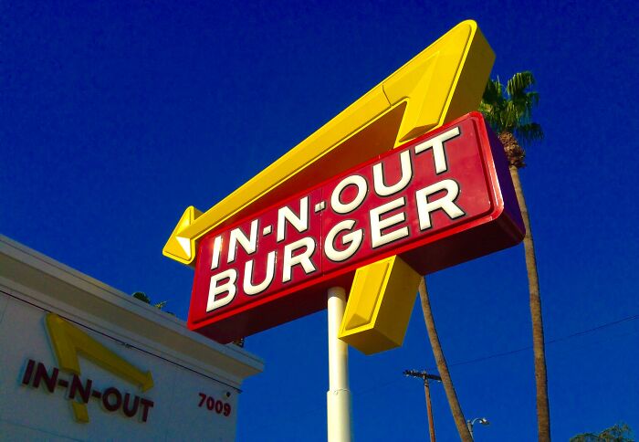 In-N-Out Burger sign against a clear blue sky, with palm trees in the background.