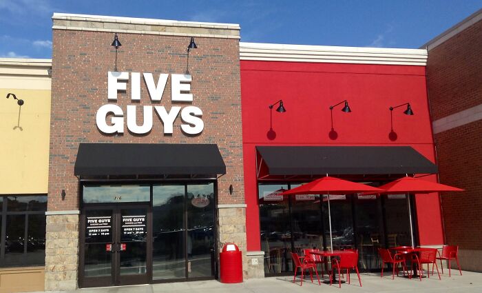 Five Guys restaurant exterior with red and yellow walls, featuring outdoor seating.