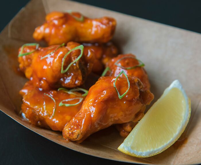 Fast food disappointment: saucy chicken wings with green onions, served with a lemon wedge in a cardboard container.