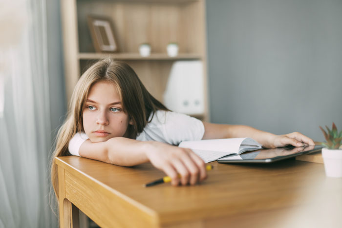Teen girl resting on a table with homework, looking pensive. Teen girl resting on a table with homework, looking pensive.