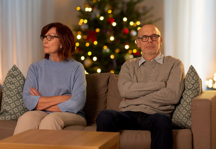 Elderly couple looking upset on a couch in front of a decorated Christmas tree, arms crossed. Elderly couple looking upset on a couch in front of a decorated Christmas tree, arms crossed.