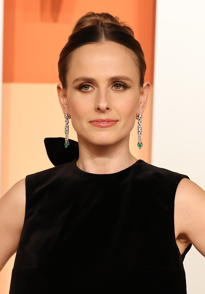Woman in a black dress with elaborate earrings, related to Timoth&eacute;e Chalamet, appearing in a vibrant setting.
