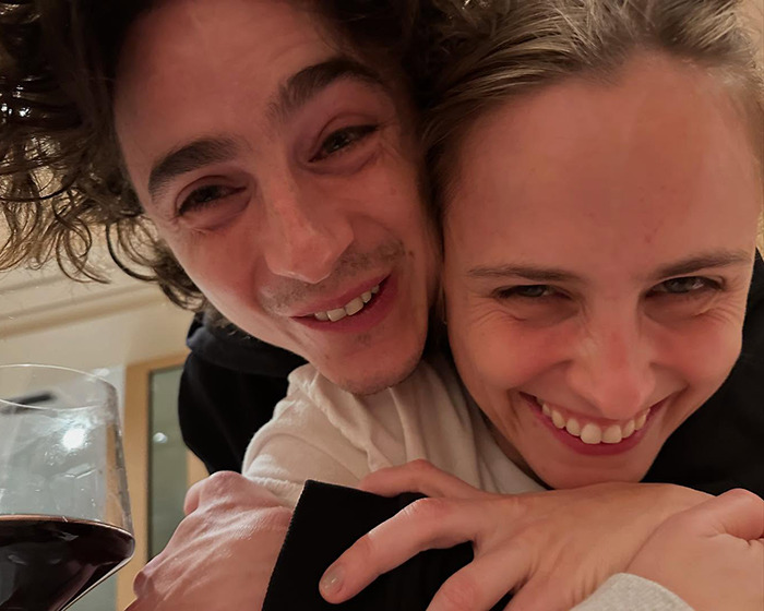 Two people smiling together closely, holding a glass of red wine.