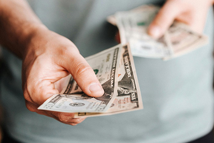 Hands holding and handing over dollar bills, illustrating financial advice from older people to those under 30.