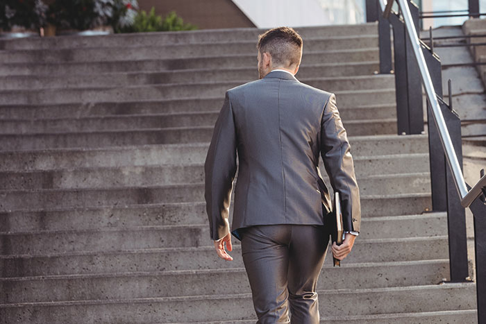 A man in a gray suit walks up stairs, holding a folder, illustrating advice for those 30 and under from older people.