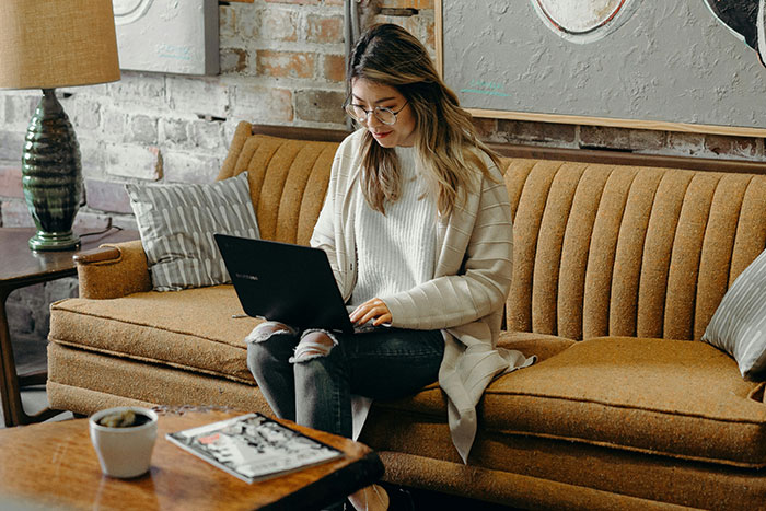 A person using a laptop on a retro couch, surrounded by home decor, capturing life insights from older generations.