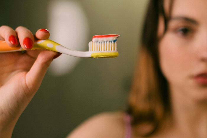 Young woman holding a toothbrush with toothpaste, highlighting life lessons from older people's advice for those under 30.