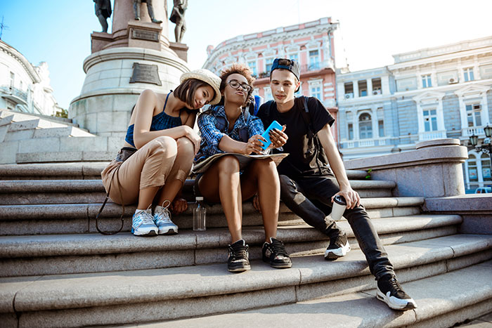Three young friends sitting on steps, enjoying a sunny day and sharing stories about life.