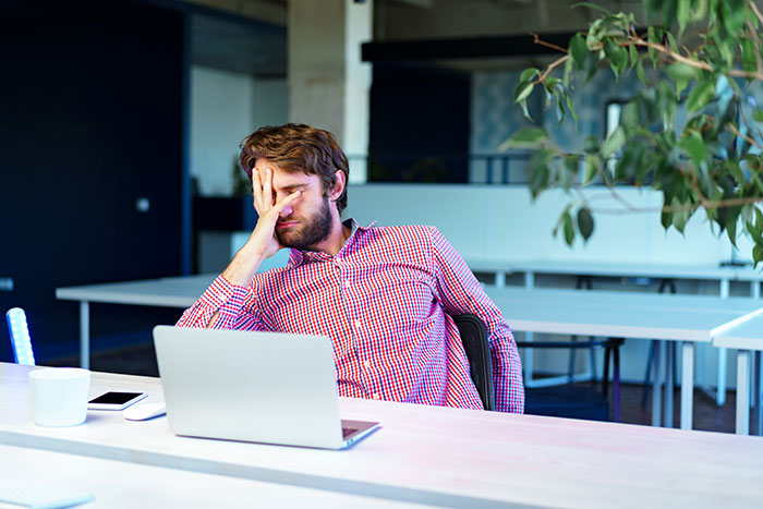 Man in red checkered shirt sitting at desk with laptop and phone, looking stressed, representing advice from older people.