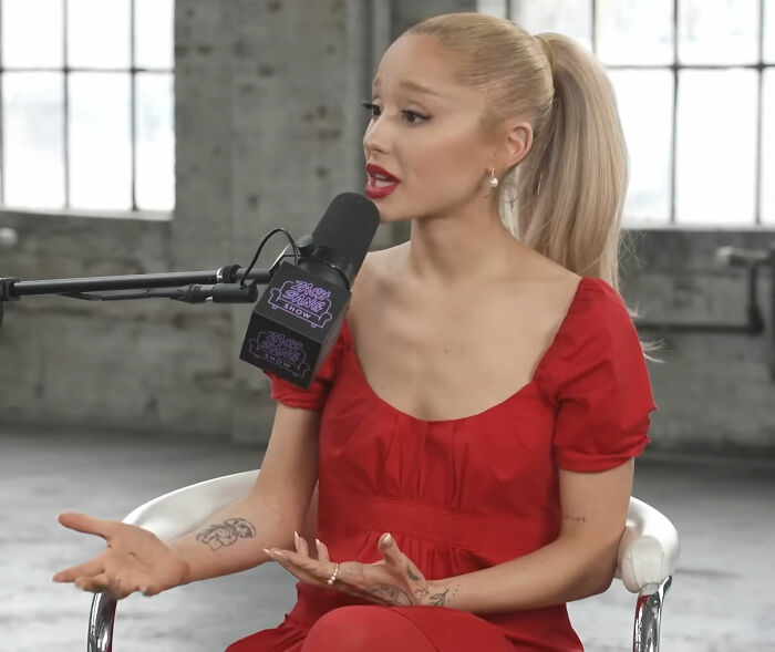 Person in red dress speaking into microphone; subject of mixed opinions on attractiveness.
