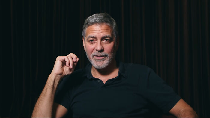 A man in a dark shirt sits against a dark background, part of a discussion on diverse celebrity attractiveness opinions.