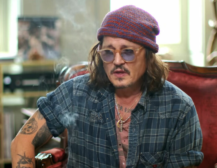 Man in casual attire with sunglasses and a beanie, sitting indoors.