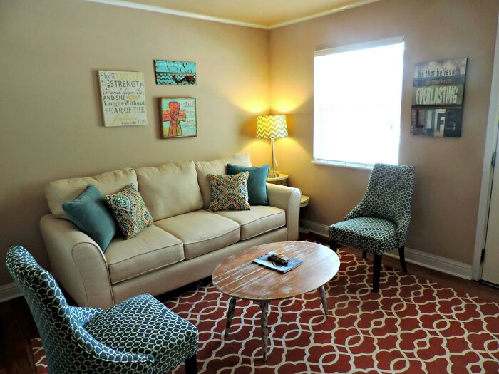 Cozy living room setup shared by first-time home buyers, featuring a beige sofa, colorful cushions, and patterned chairs.