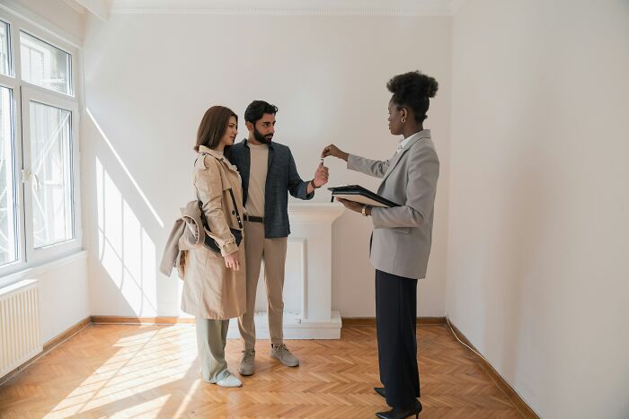 A couple receives keys from a real estate agent in an empty room, symbolizing first-time home buyer success.