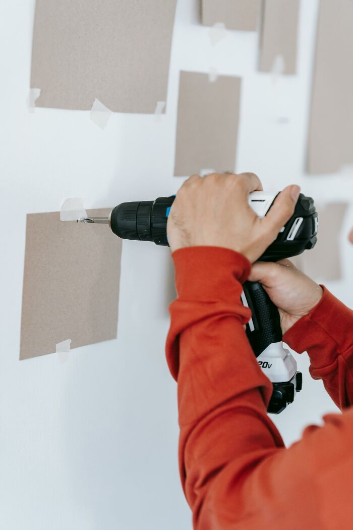 Person in red shirt using a drill on a wall, sharing insight into first-time home buyer challenges.
