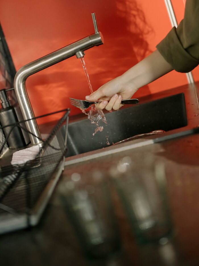 Person washing a fork under running water in a kitchen sink, illustrating a scene related to rage quitting a job.
