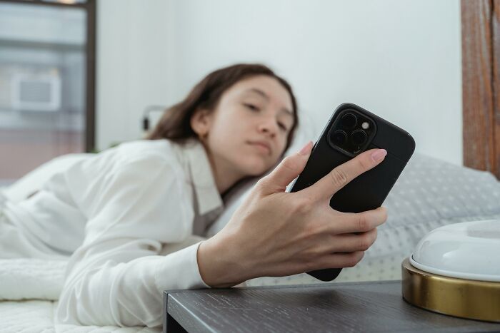 Woman lying on bed, holding a phone, possibly reflecting on a job rage quit moment.