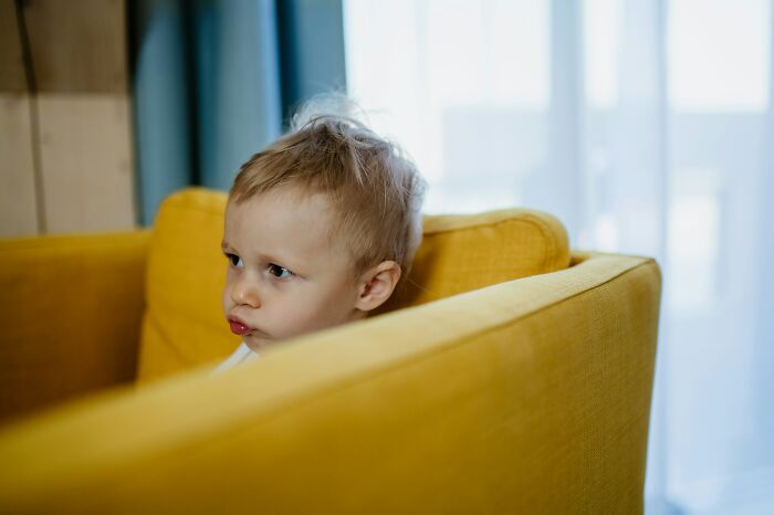 Toddler sitting in a yellow chair, looking thoughtful in a bright room, symbolizing childfree decision considerations.