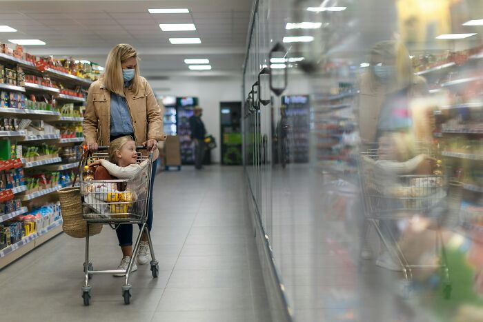 Woman with child in a shopping cart at a grocery store aisle, reflecting on life's choices without kids.