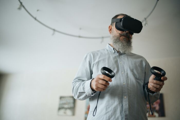 Bearded man with VR headset and controllers, exploring virtual reality at home, symbolizing lifestyle choices without kids.