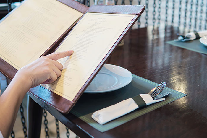 A person pointing at a menu in a restaurant, highlighting traditional dining choices often appreciated by older generations.