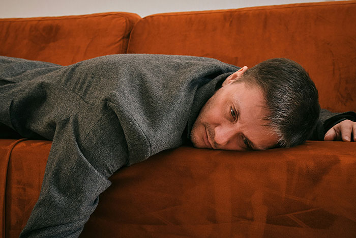 Man in a gray jacket lying face down on an orange sofa, reflecting on what older generations got right.