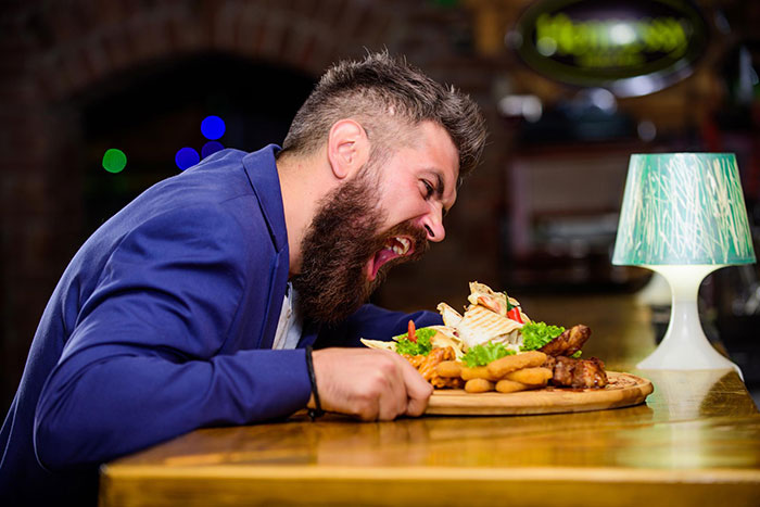 Bearded man in a blue jacket enthusiastically eating a large platter, representing things boomers got right.