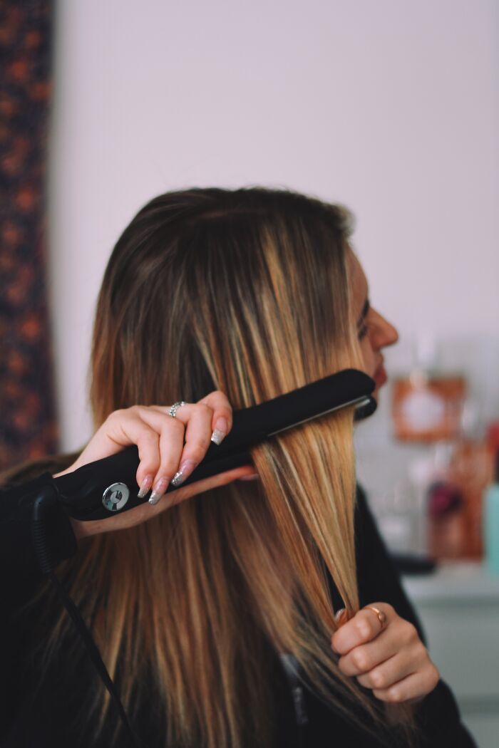 Person using a hair straightener, engaging in unprofessional behavior at work.