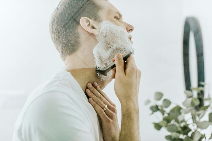 Person shaving with foam, using a razor in front of a mirror, illustrating unprofessional behavior seen at work.