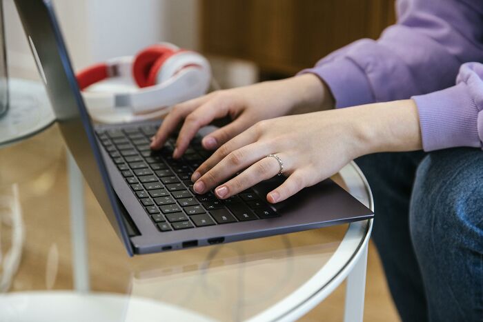 Person typing on a laptop at work, with red headphones on the table, highlighting unprofessional work settings.