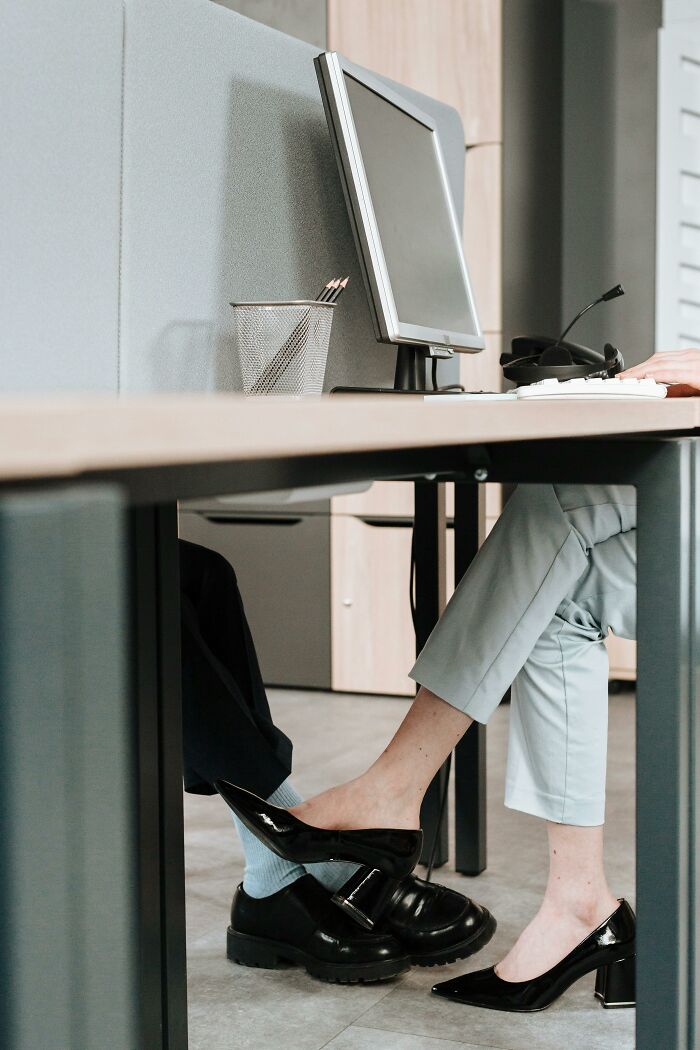 Two colleagues playfully engaging under a desk, showcasing unprofessional work behavior.