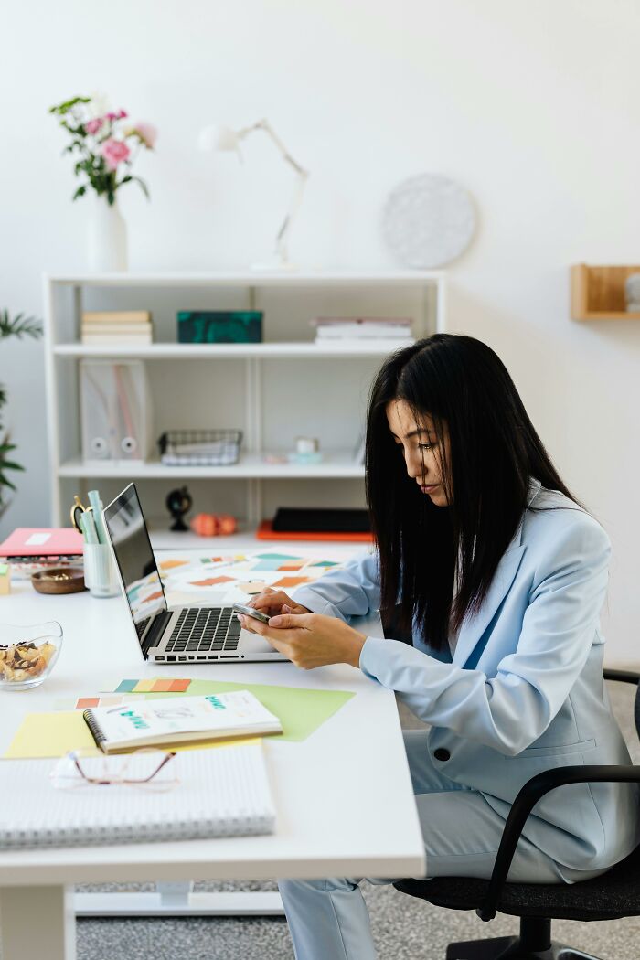 Professional woman in light blue suit using smartphone at a desk, representing workplace scenarios.