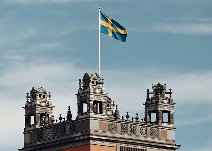 Swedish flag atop a historic building against a cloudy sky, related to countries people make fun of.