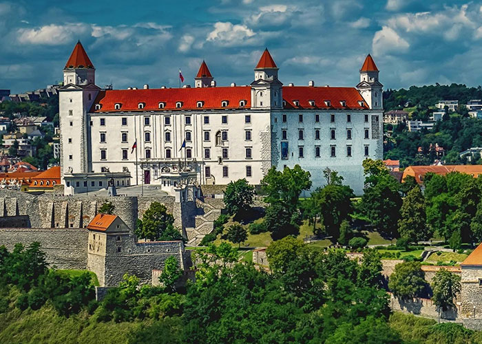 Historic castle in Slovakia framed by lush greenery against a blue sky.