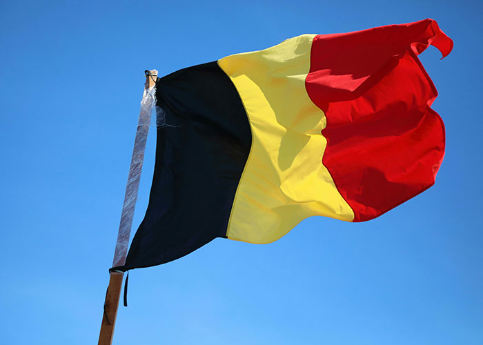 Belgian flag waving against a clear blue sky, highlighting a country often made fun of.