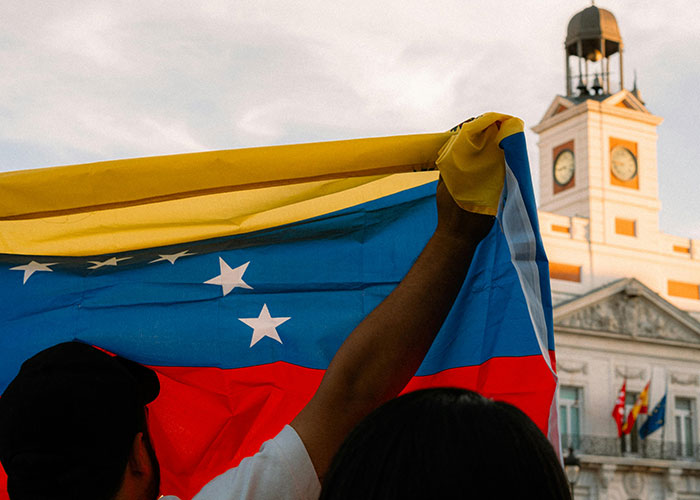 Person holding Venezuelan flag near a clock tower, representing a country often made fun of.