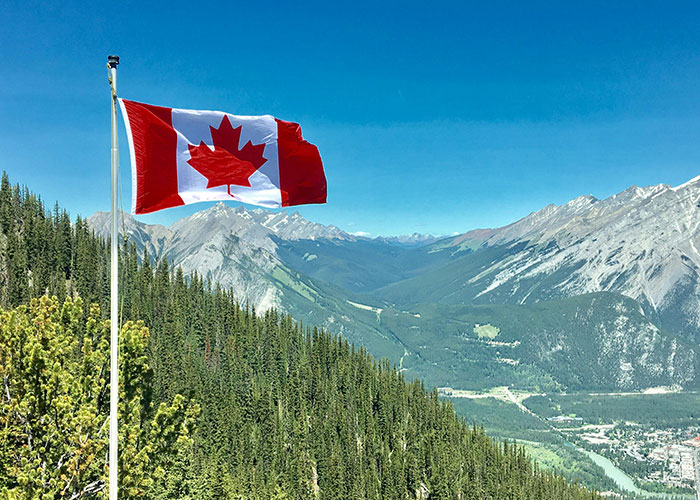 Canadian flag waving over a mountain landscape, related to countries people make fun of.