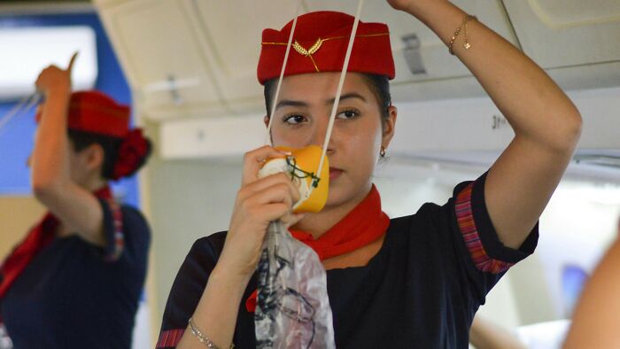 Flight attendant demonstrating safety mask, challenging travel misconceptions.