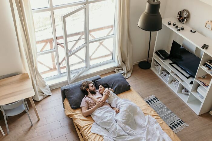 Couple lying together in a cozy bedroom with sunlight streaming through a window.