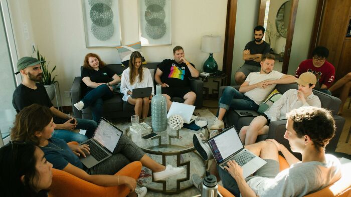 A group of people in a living room, discussing with laptops, showcasing signs of intelligence.