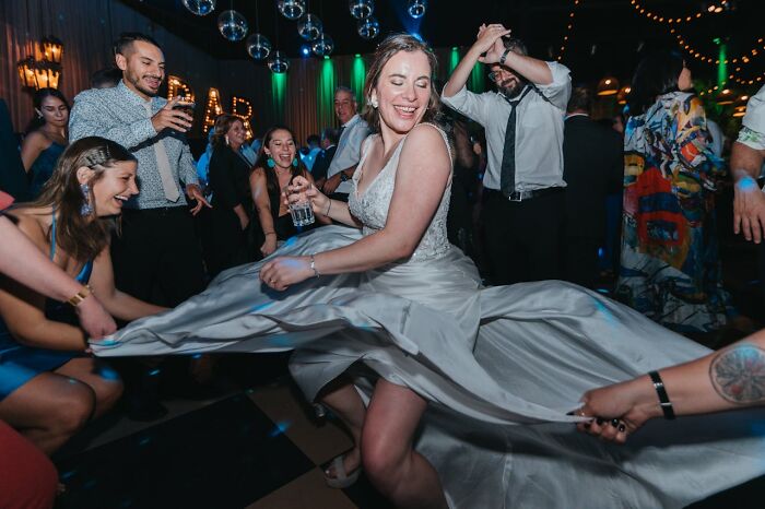 Wedding dance gone wrong, guests in laughter as bride spins, holding her dress, capturing a bridal party mishap moment.