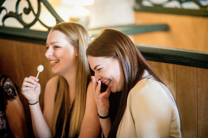 Two women laughing together, seated in a cozy cafe, showing subtle signs of intelligence through their expressions.