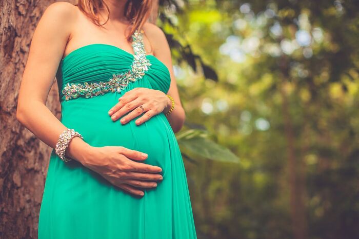 Pregnant woman in a teal dress with floral detail, holding her belly outdoors, relating to wedding mishaps.