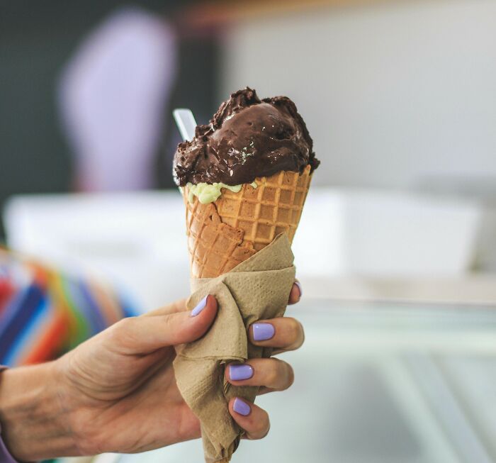 A hand holding a waffle cone with chocolate ice cream, wrapped in a napkin, representing foods some find unappealing.