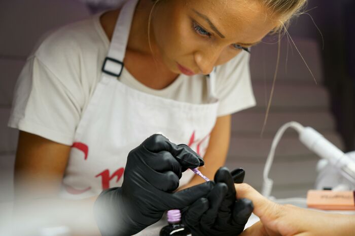Woman in an apron applying nail polish, concentrating, representing tales of someone making things worse.