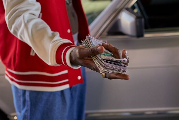 Person in a red jacket holding a large stack of cash, symbolizing easily made money.