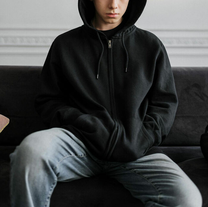 Person in a black hoodie and jeans sitting on a couch, conveying a judgmental mood.