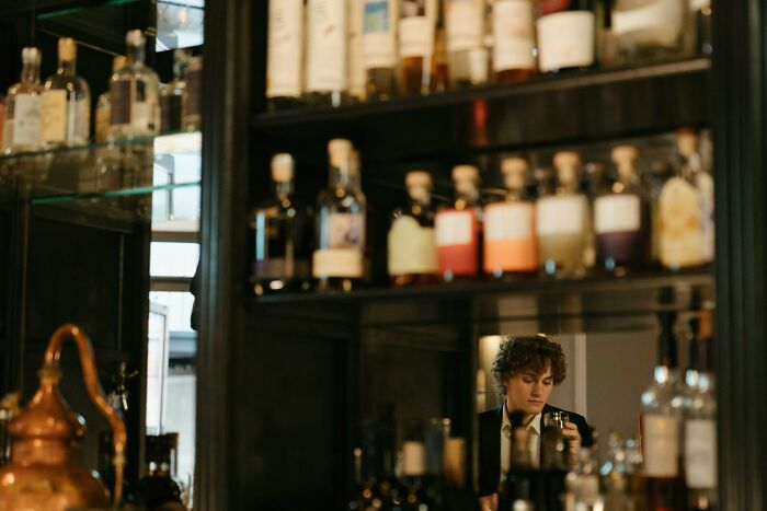 Individual standing at a bar, reflected through bottles, evoking a wedding nightmare scenario.