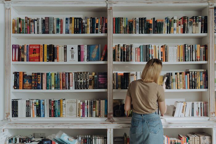 A person browsing a large bookshelf, possibly indicating intelligence through a keen interest in books.